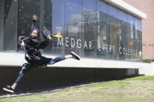 Female student in front jumping in front of Bedford building