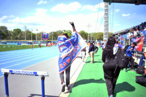 Chrisnel Nicolas walks off the track at Icahn Stadium draped by the championship banner after the Medgar Evers College men's outdoor track and field team captured the conference title on May 3, 2025. (Nick Masuda/Office of Communications)