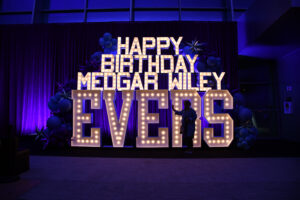 Shakema Antoine poses in front of the massive sign celebrating the 100th birthday of Medgar Wiley Evers. (Photo by Maritza Argueta/Office of Communications)